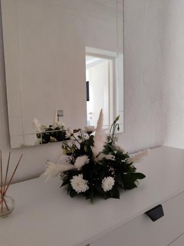 a bathroom counter with a mirror and a bouquet of white flowers at Apartman ASKA in Višegrad