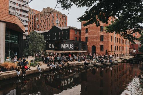 a crowd of people sitting on a sidewalk next to a river at Kampus in Manchester