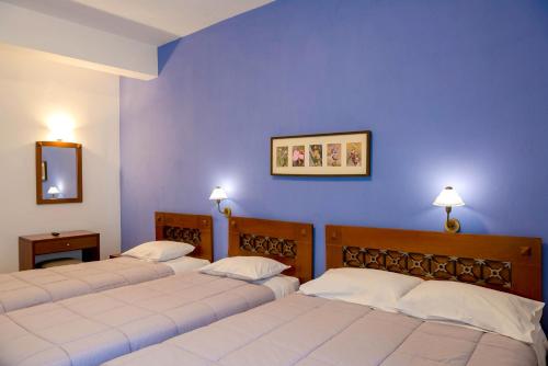 3 camas en una habitación con paredes azules en Artemis Hotel, en Delfos