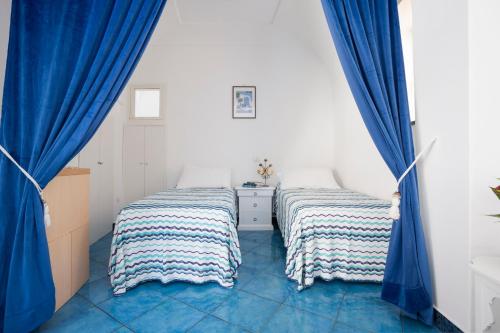 two beds in a room with blue curtains at YourHome - La Vedetta Sea View in Positano