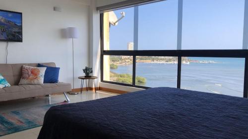 a bedroom with a bed and a couch and a large window at Apart. con aire, frente al mar in Porlamar