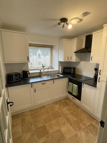 a kitchen with white cabinets and black counter tops at Daisy Cottagee in Alyth