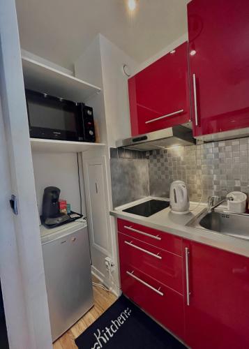 une petite cuisine avec des armoires rouges et un évier dans l'établissement Appartement 12 min Paris - Parking Privé Gratuit - Wifi - Netflix - Balcon, à Enghien-les-Bains