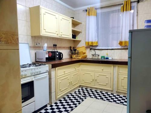 a kitchen with yellow cabinets and a black and white tile floor at SwanLakeview3br, Wi-Fi, Netflix, Balcony, Sunset. in Kisumu
