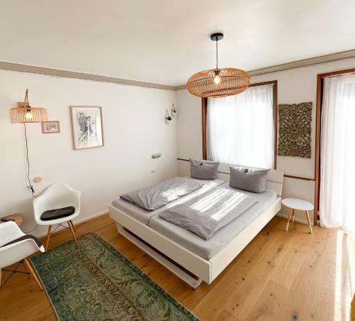 a white bedroom with a bed and a chair at Hacienda Rooms in Friedrichshafen