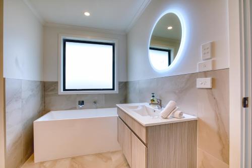 羅托魯阿的住宿－Stylish 4 Bedroom house Brand New in Rotorua，带浴缸、水槽和镜子的浴室