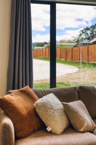 a couch with pillows sitting in front of a window at Stylish 4 Bedroom house Brand New in Rotorua in Rotorua