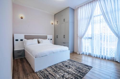 a white bedroom with a bed and a large window at Amnen Apartments in Addis Ababa