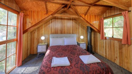 a bed in a room with wooden walls and windows at Crayfish Creek Van & Cabin Park in Crayfish Creek