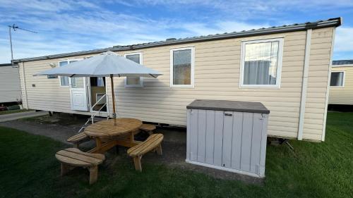 a picnic table and an umbrella next to a house at Cozy Private Static Caravan at Llyons Robin Hood - Silver Birch Way 11 in Rhyl