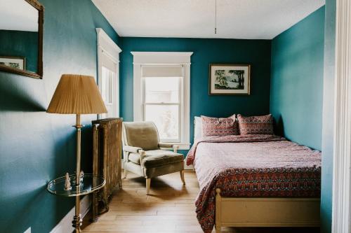 a bedroom with blue walls and a bed and a chair at Retro Gem Box Victorian Steps from Irvine Park in Saint Paul