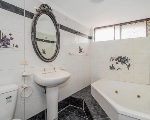 Baño blanco con lavabo, bañera y espejo en Queen Size Bedroom Near Sawn River en Perth