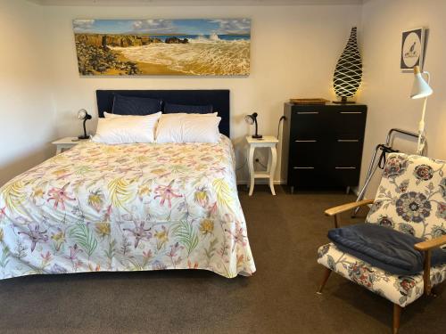 a bedroom with a bed and a chair and a painting at Brophys Beach Studio in Whitianga