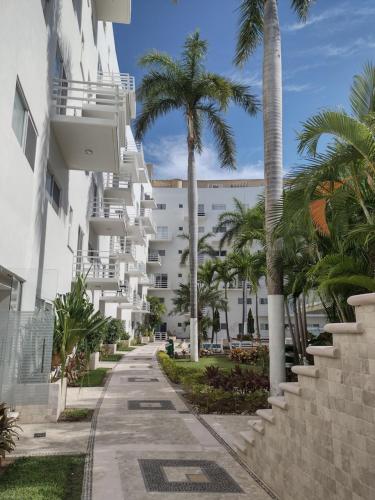 a street in front of a white building with palm trees at Departamento en Acapulco Diamante in Acapulco