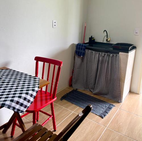 a kitchen with a table and a red chair and a sink at Cabana Monte Trigo in São Francisco do Sul