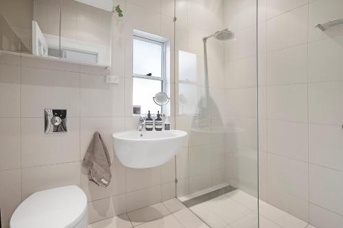 a white bathroom with a sink and a shower at Beautiful victorian garden apartment, with pool. in Sydney