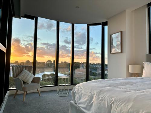 a bedroom with a bed and a chair in front of windows at Skygarden Luxury Condo in Glen Waverley