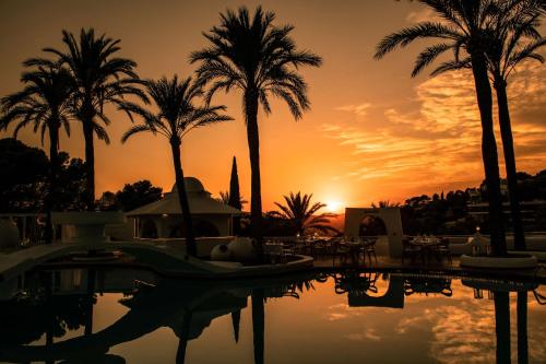 una piscina con palmeras y una puesta de sol en el fondo en Hilton Mallorca Galatzo, en Paguera