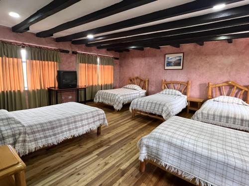 Hotel Achik Wasi في Saraguro: غرفة بثلاث اسرة وطاولة وتلفزيون