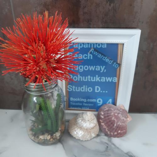 a red flower in a mason jar next to a picture at Papamoa Beach Hugoway, Pohutukawa Studio Deluxe, Close beach, free parking in Papamoa