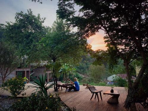 a woman sitting on a wooden deck in a garden at Sa Moc - La Maison House & Bungalow in Sa Pa