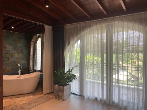La salle de bains est pourvue d'une baignoire et d'une grande fenêtre. dans l'établissement TROPICAL HOUSE RIVERSIDE RETREAT, à Thuan An
