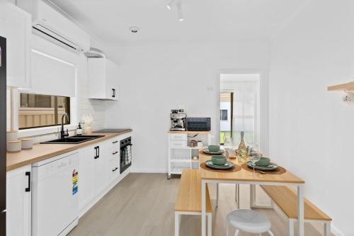a kitchen with white cabinets and a wooden table at Easts Beach Escape - A Relaxed Coastal Cottage in Wollongong