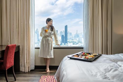 a woman standing in front of a window with a tray of food at Marriott Executive Apartments Sukhumvit Park, Bangkok in Bangkok