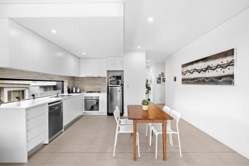 a white kitchen with a wooden table and chairs at New Modern 2BR 2baths Apt in Homebush Sleeps 6 in Sydney