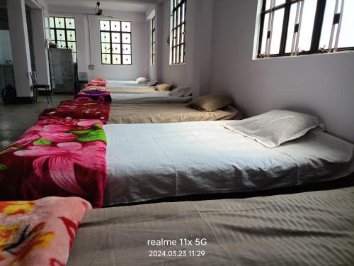 Muzaffarpur Guest House في مظفربور: صف من الأسرة في غرفة مع نوافذ