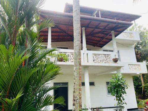 a white house with a balcony and palm trees at Susha Happy One First Floor Apartment in Hikkaduwa