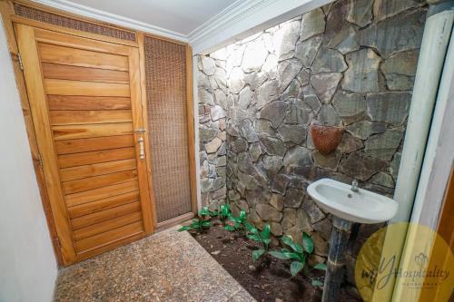 a bathroom with a stone wall and a sink at Joglo Garut Cottage Syariah by My Hospitality in Bojongsalam