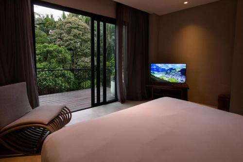 a bedroom with a bed and a large window with a television at The Ning Resort Ubud in Ubud