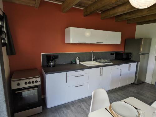 a kitchen with white cabinets and an orange wall at Au Bonheur des Makes in Saint-Louis