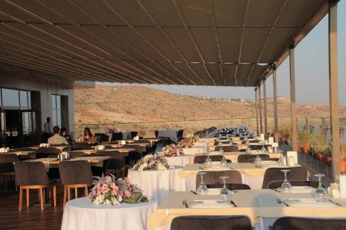 a large banquet hall with tables and chairs with mountains in the background at Windyhill Hotel in Elazığ