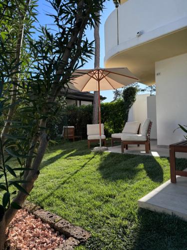 a patio with an umbrella and chairs and grass at Villa Usignolo in Lignano Sabbiadoro