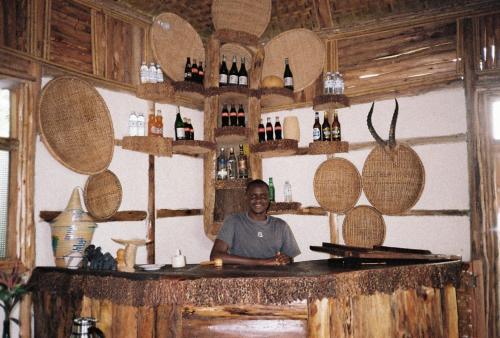 un homme assis au bar dans une pièce avec beaucoup de bouteilles de vin dans l'établissement Bwindi My Home, à Kinkizi