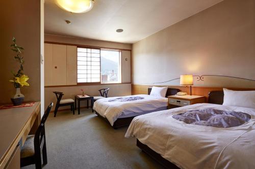 a hotel room with two beds and a desk at Hotel New Tsuruta in Beppu
