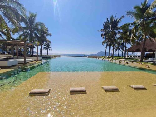 a swimming pool with palm trees and a beach at Bonito departamento pie de playa en el mejor condominio de manzanillo, Ponto Horizonte. Hermosa vista, hasta para 8 personas. Ambiente familiar. in Manzanillo