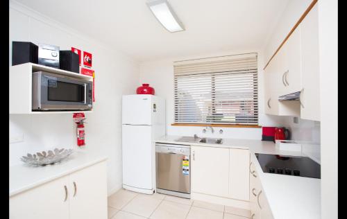 a white kitchen with a refrigerator and a microwave at Mildura Holiday Villas in Mildura
