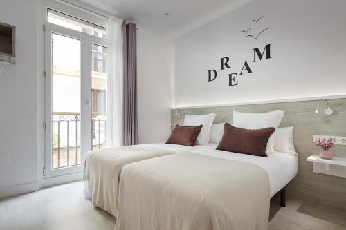 two beds in a white room with a window at Pension El Puerto in San Sebastián