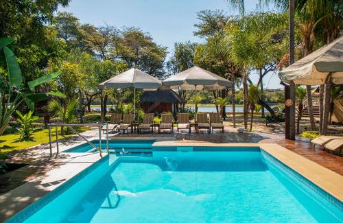 a swimming pool with tables and chairs and umbrellas at Hakusembe River Camping2Go 