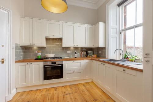 a kitchen with white cabinets and a sink and a window at Stylish Victorian Apartment's close to the Botanical gardens, Free parking! in Edinburgh