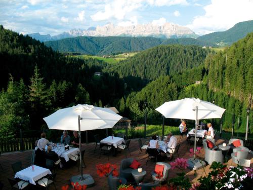 a patio with tables and umbrellas with mountains in the background at Ganischgerhof Mountain Resort & Spa in Nova Ponente