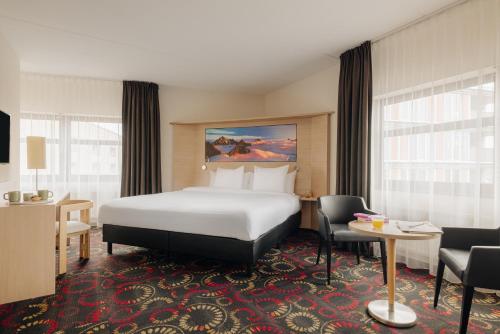 City Hotel Hengelo في هينغلو: غرفة فندقية بسرير وطاولة وكراسي