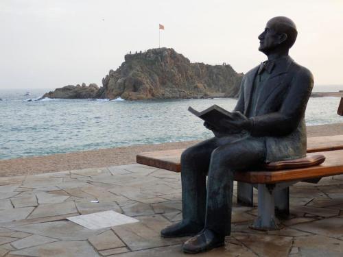 a statue of a man sitting on a bench reading a book at Apartamento Blanes playa (Costa Brava) in Blanes