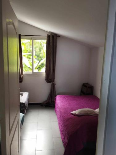 - une petite chambre avec un lit violet et une fenêtre dans l'établissement Clos du Soleil Levant, à Sainte-Rose