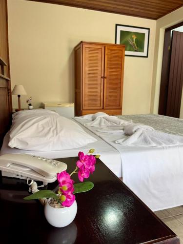 a bed with a table with a phone and flowers on it at Pousada Finlândia in Penedo