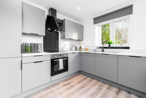a white kitchen with white cabinets and a wooden floor at Smethwick Deluxe 2 Bedroom Aparetment - Secure Parking - Balcony - Rated Exceptional - 9MC in Birmingham