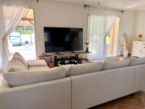 un gran sofá blanco en una sala de estar con TV en Villa les cigales - Paisible avec piscine en Mas-Saintes-Puelles